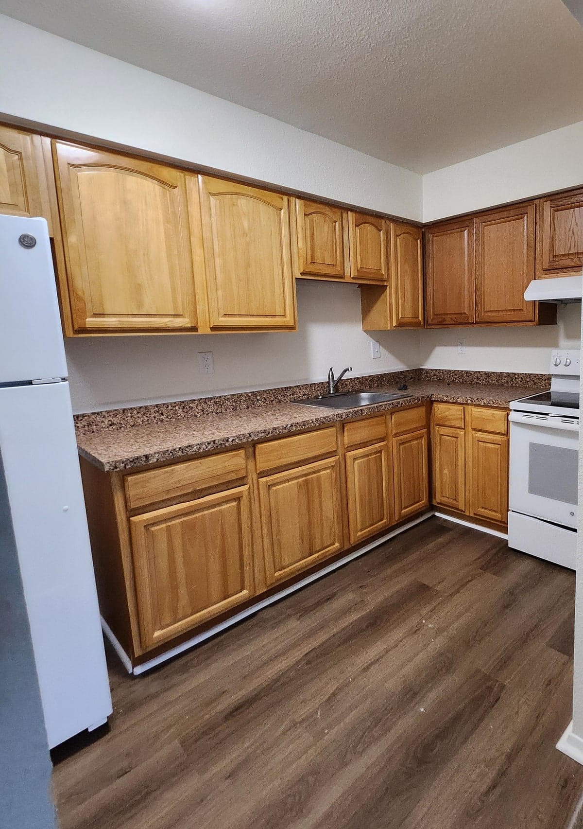 An oak-cabinet kitchen at Prince Frederick Village with a white electric range, a double stainless sink, and wood-look plank flooring