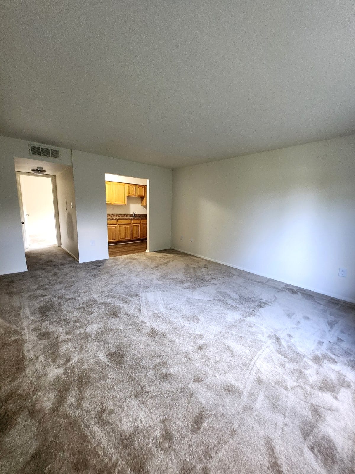A freshly carpeted living room at Prince Frederick Village, opening through a wide pass-through into the oak kitchen